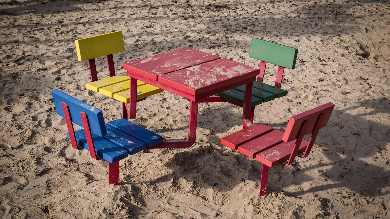 Quatre bancs de couleurs différentes autour d’une même table, sur le sable