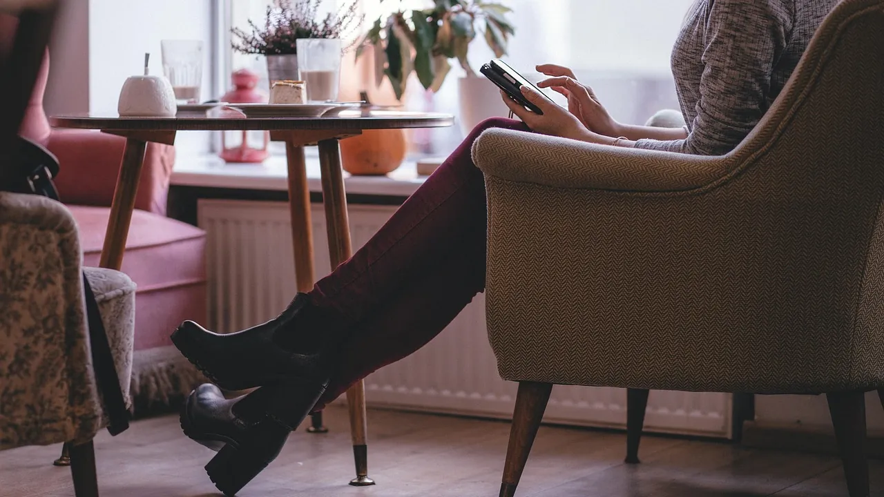 Une personne installée dans un fauteuil près de la fenêtre, un téléphone à la main