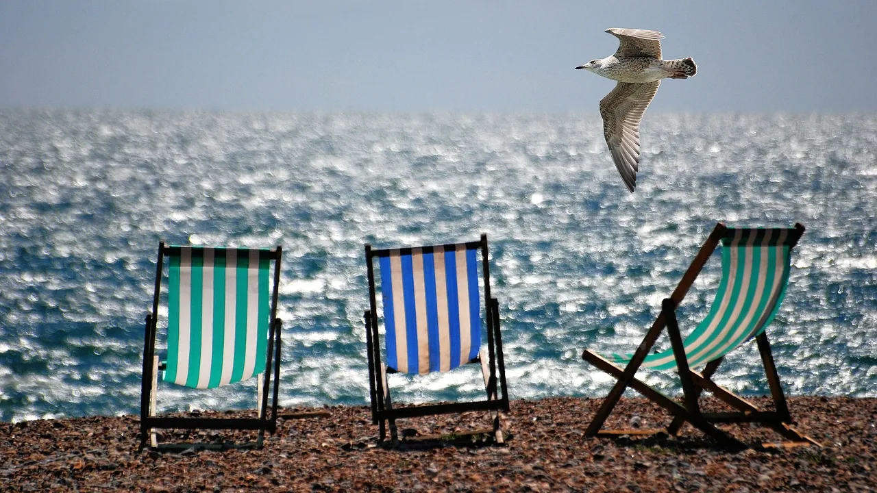 Trois chaises longues rayées face à la mer, sur une plage de galets